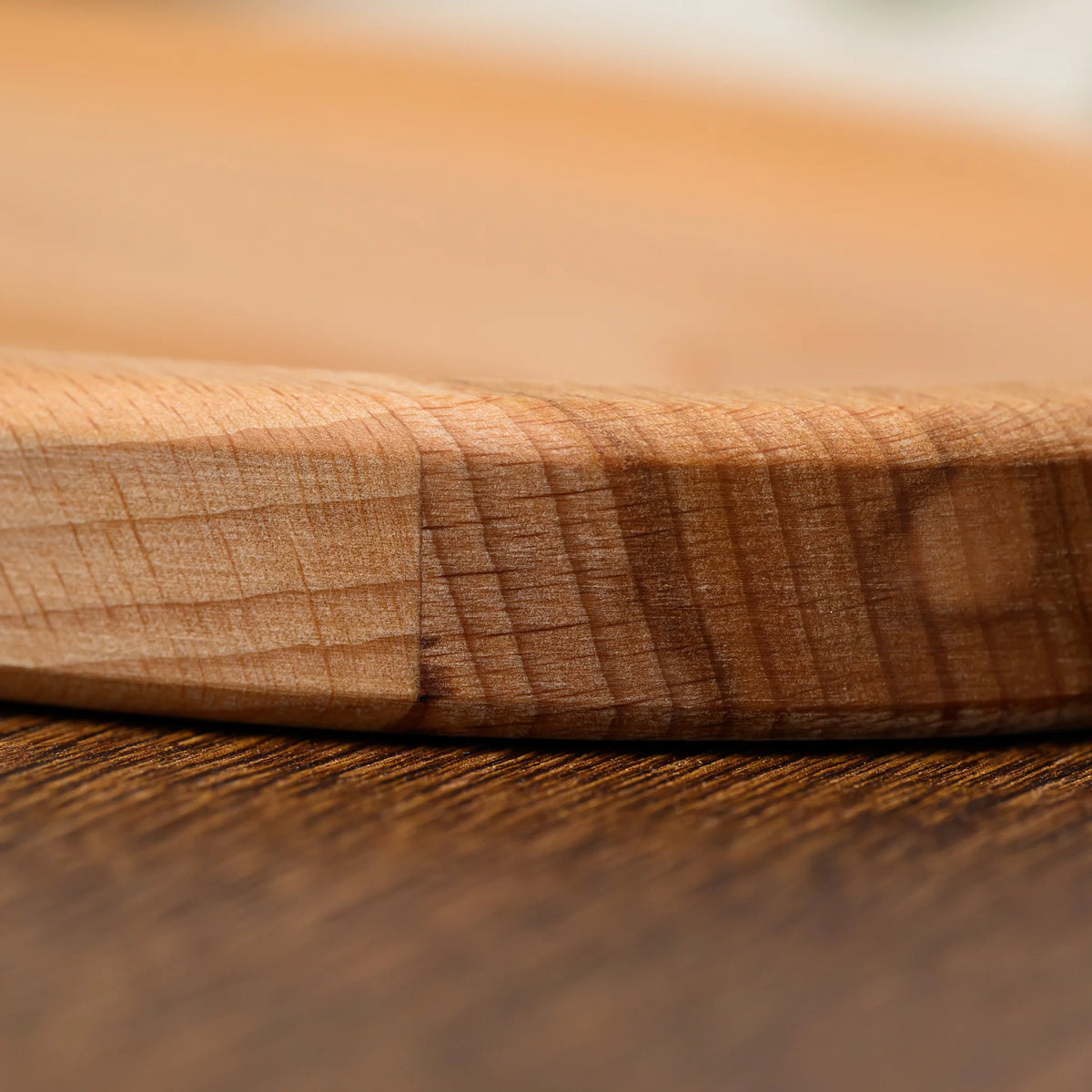 Close-up of the rounded end and raised rim of the beech wood oval serving board, showing natural grain
