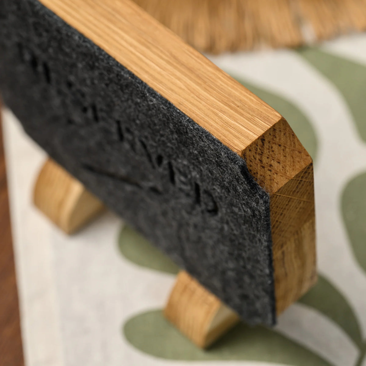 A macro side view of the felt panel edge and oak leg of a Reserved table sign, seen closely at an angle