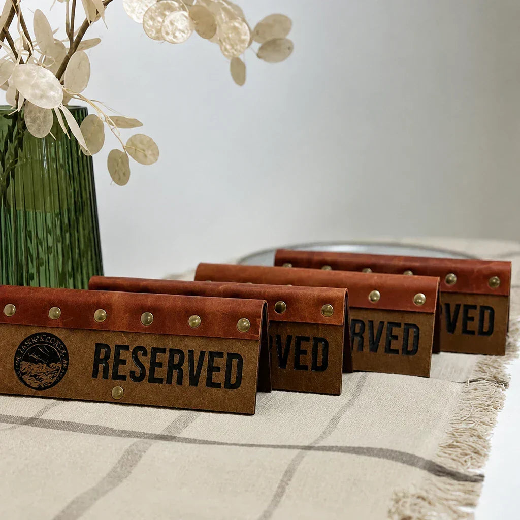 Vintage-style leather reserved table signs with brass rivets and cutout lettering for cafes and restaurants.