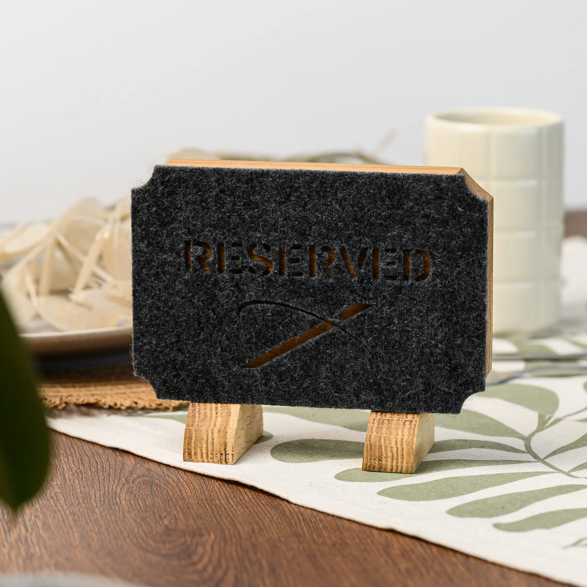 A Reserved table sign with die-cut felt lettering standing on two oak legs on a set restaurant table