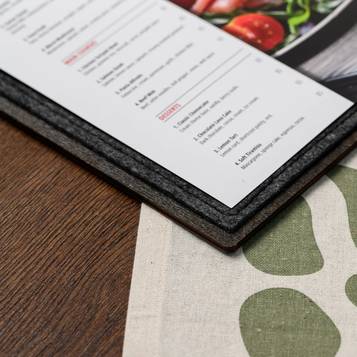 A close-up of the felt-covered corner of a menu board resting on a cream linen tablecloth, styled nearby 