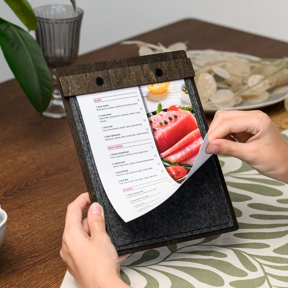 Hands holding a felt menu board, lifting the printed page that is clamped under the screw-fastened bar 