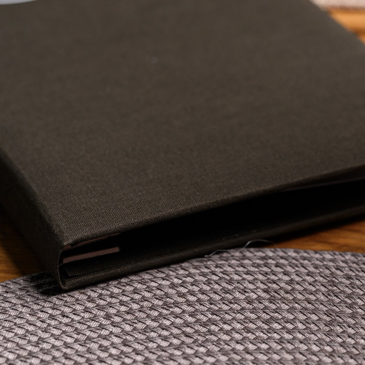 Close-up of a closed espresso-brown textile menu folder spine standing upright against a blurred background