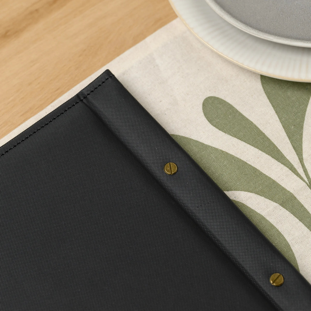 Close-up of slotted brass screws on the back cover of a black menu cover with a fine textile-like faux leather finish