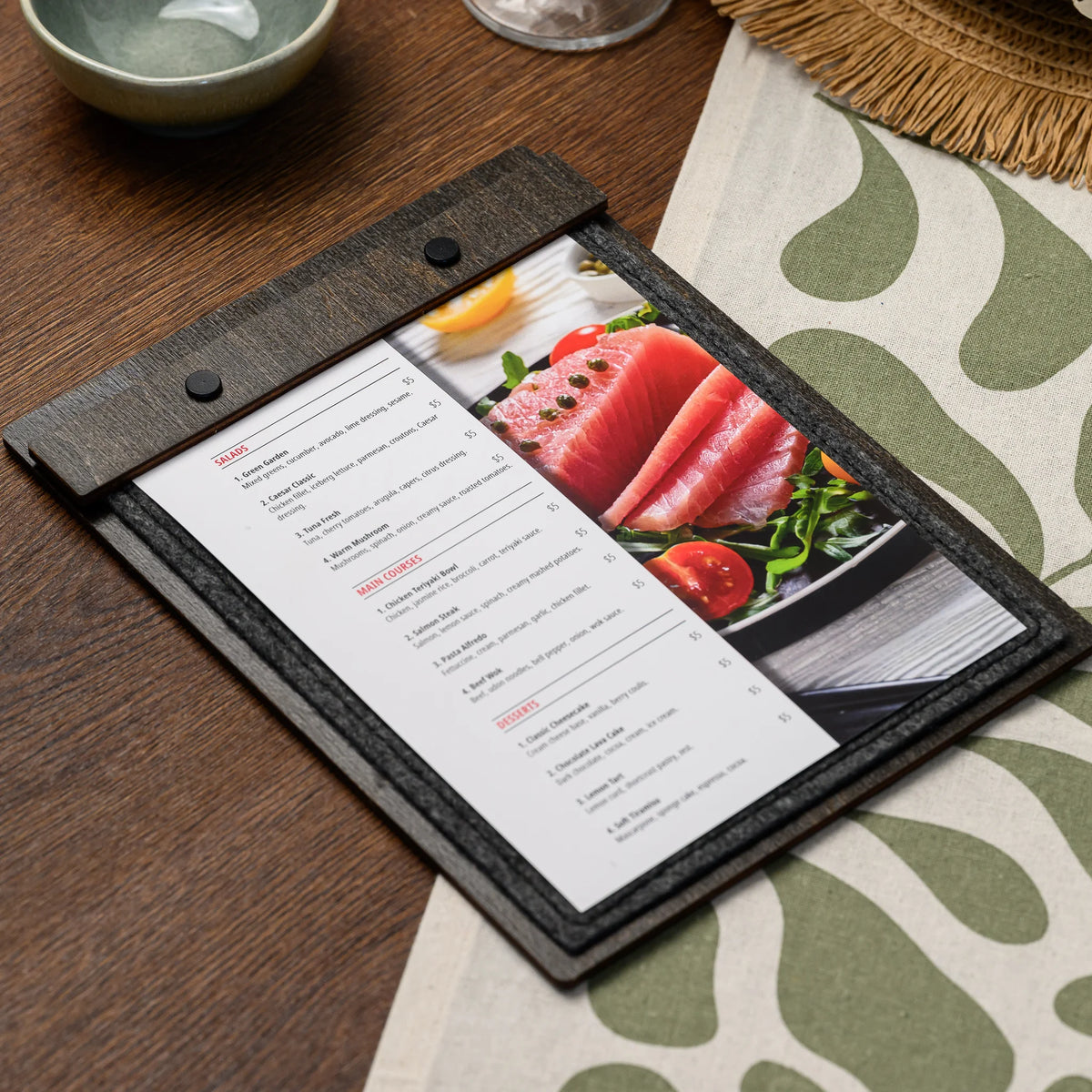 A felt menu board lying open on a set restaurant table, showing a printed page held under the clamp bar 