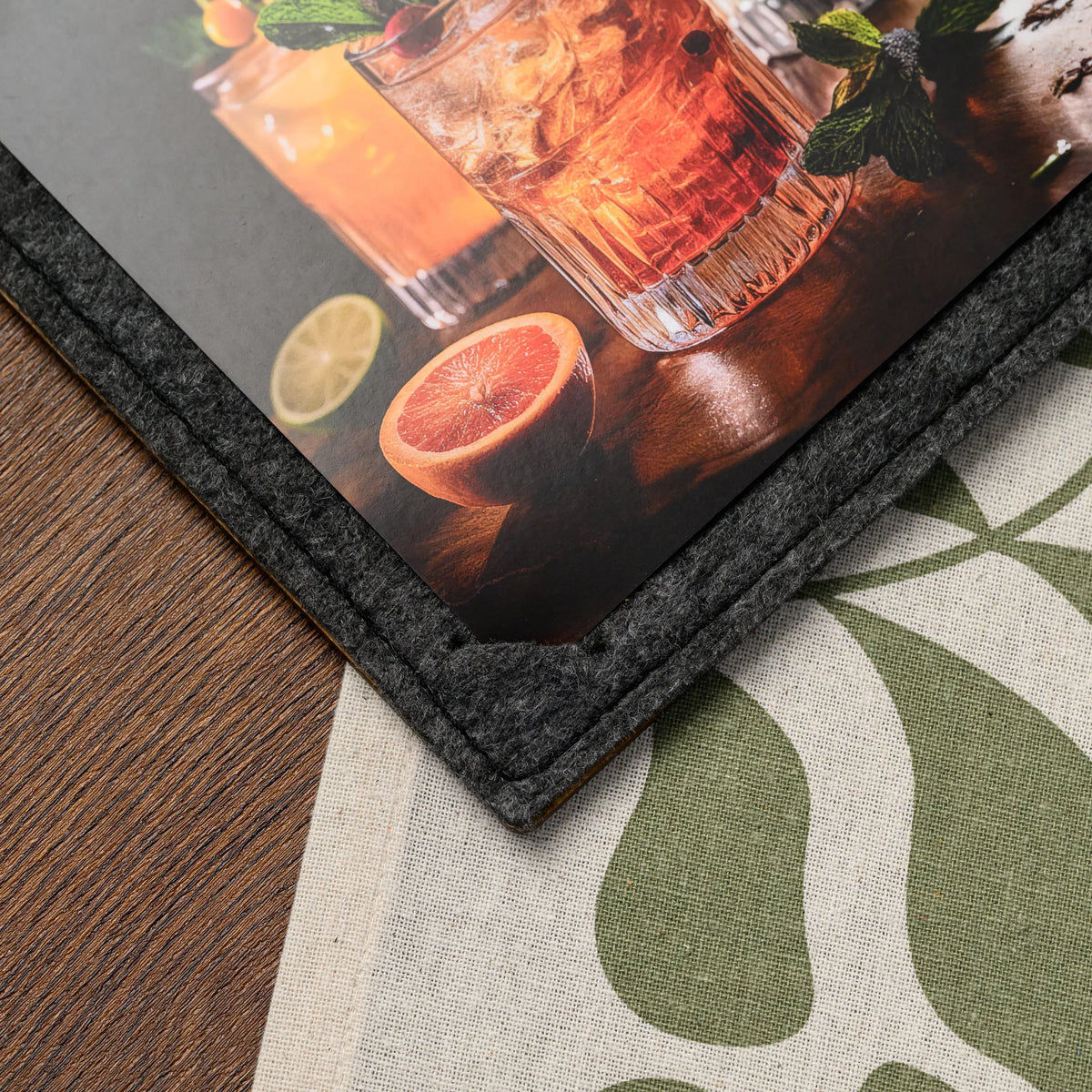 A close-up of a corner slot on the felt clipboard holding a printed menu page in place, seen at an angle 