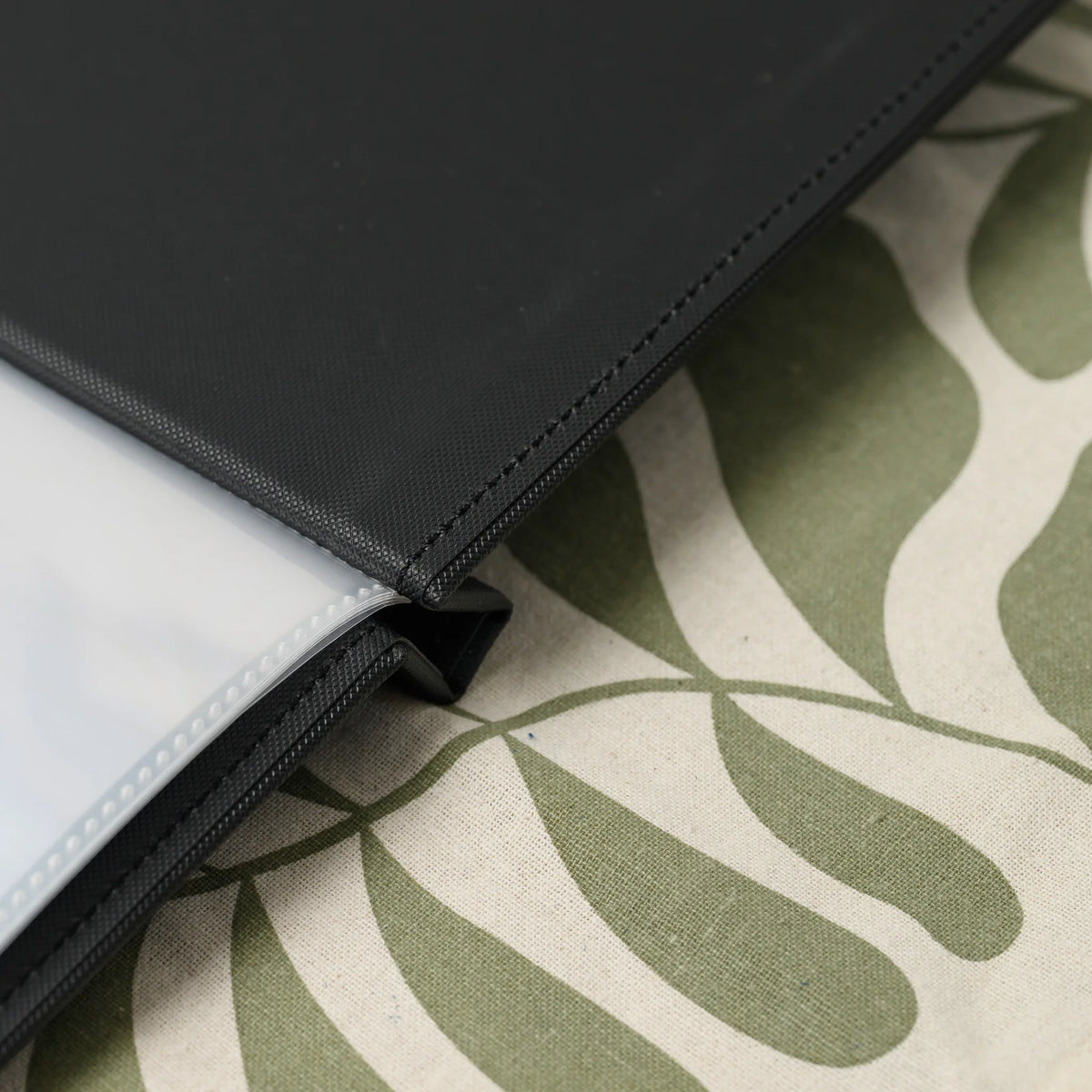 Close-up of the spine of a black textured menu cover with a stack of clear plastic sleeves held between the covers