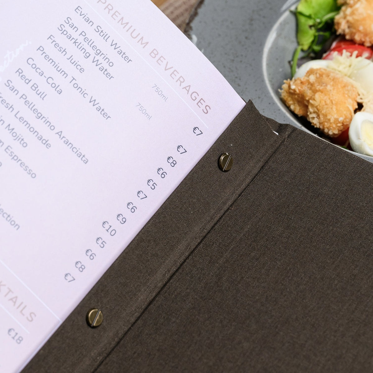 Close-up of a lavender menu page edge with a perforated dot pattern beside a blurred plate of fresh salad