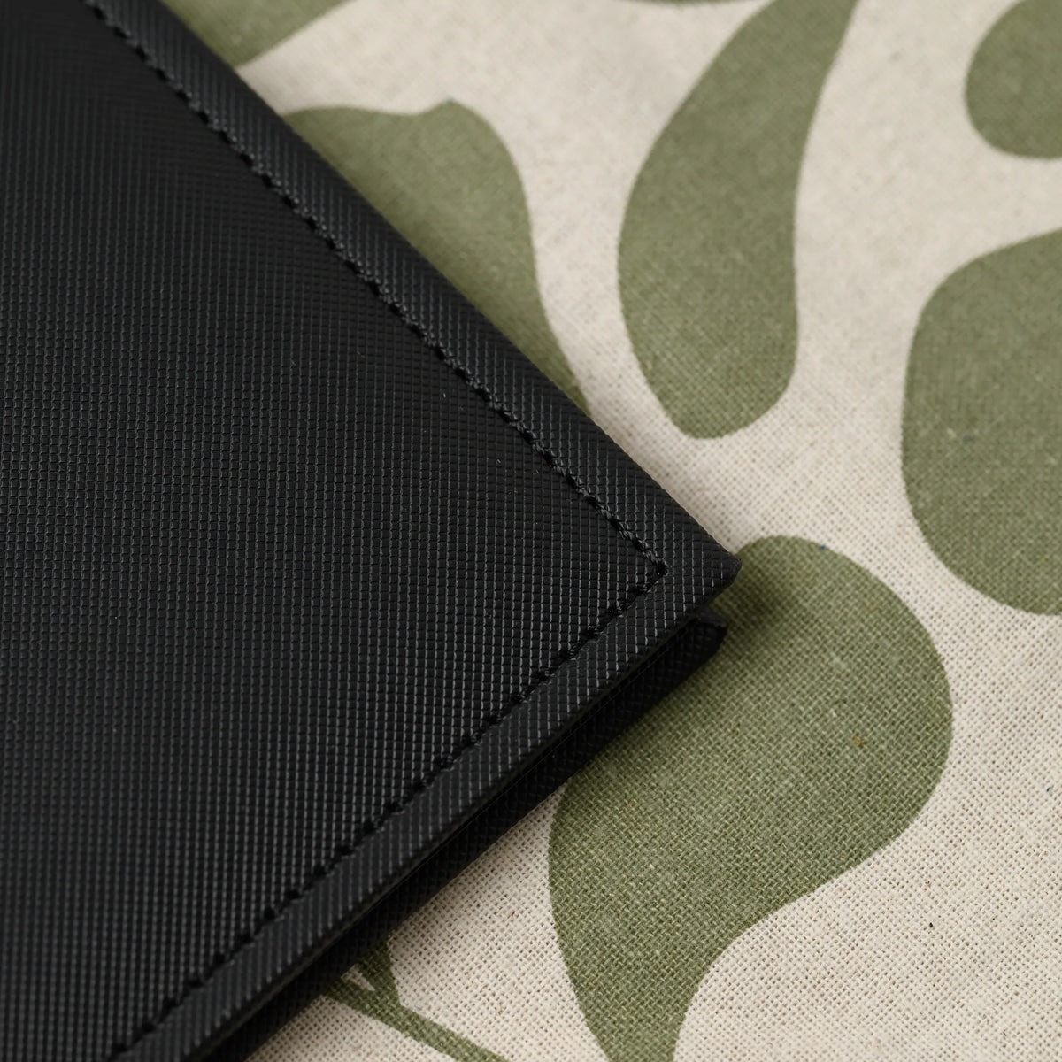 Macro view of the stitched corner of a black Nadir faux leather menu cover showing the fine woven surface texture
