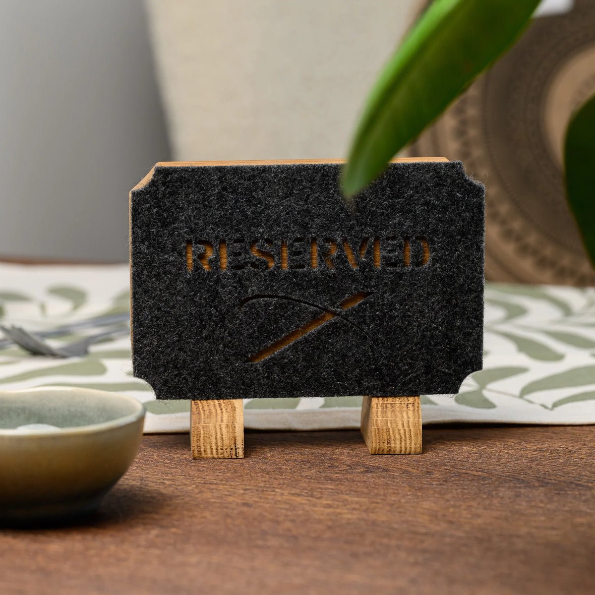 A close-up view of a Reserved table sign with felt cutout lettering, a green leaf visible in the frame