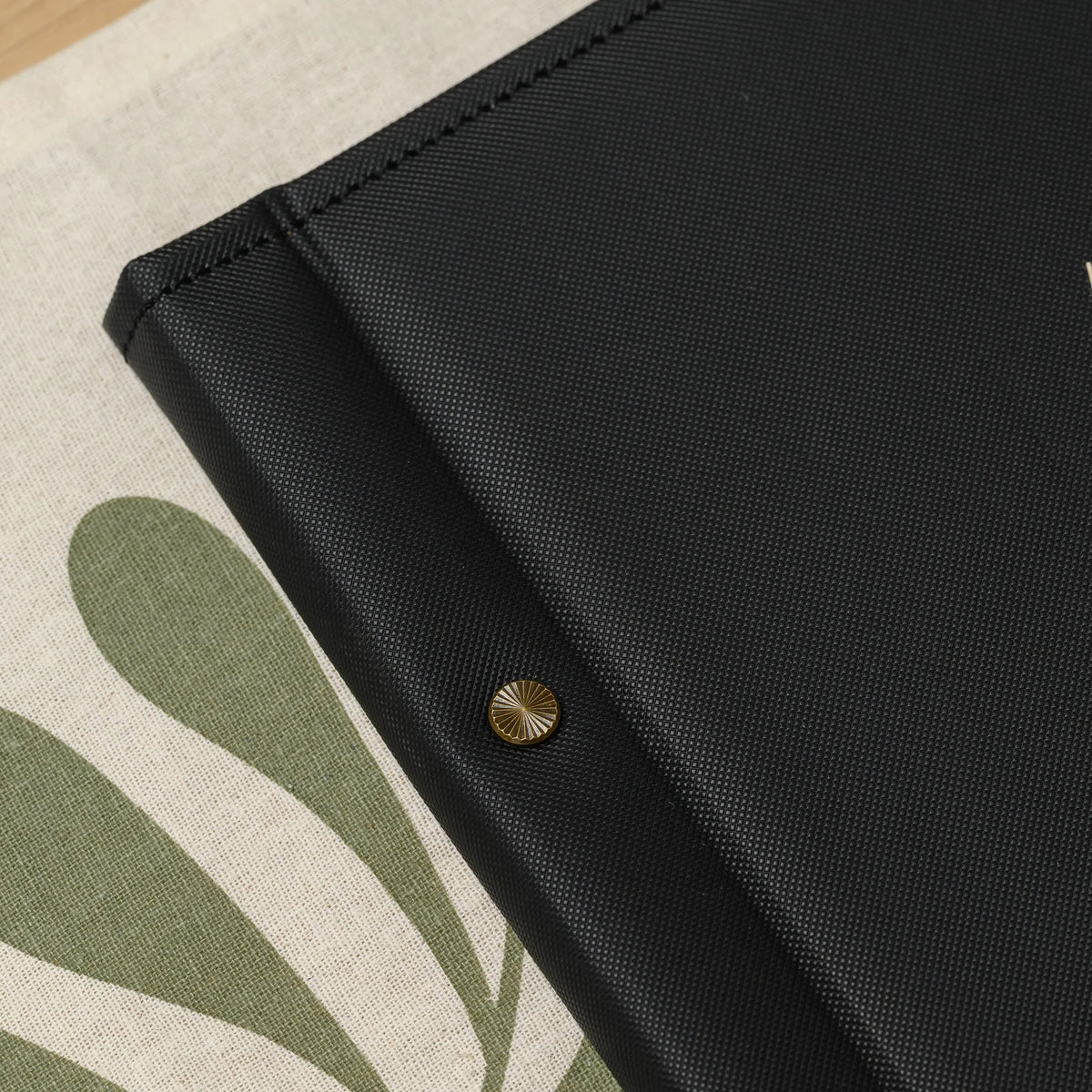 Close-up of a decorative sunburst brass screw head on the textured spine of a black faux leather menu cover