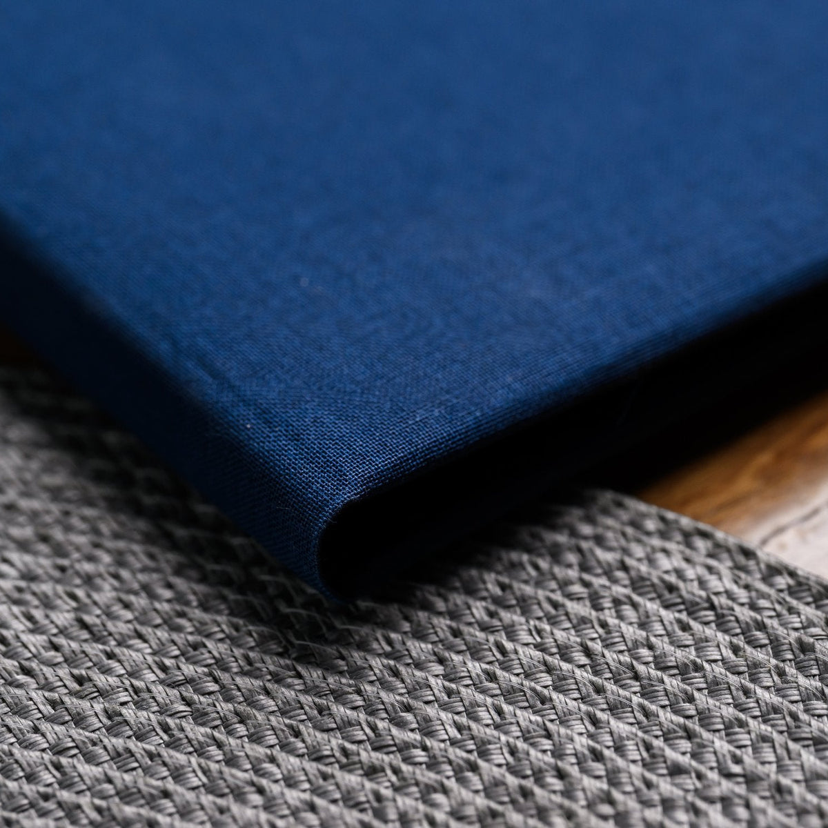 Closed navy textile menu folder lying flat diagonally on a grey knit-textured woven placemat on the table