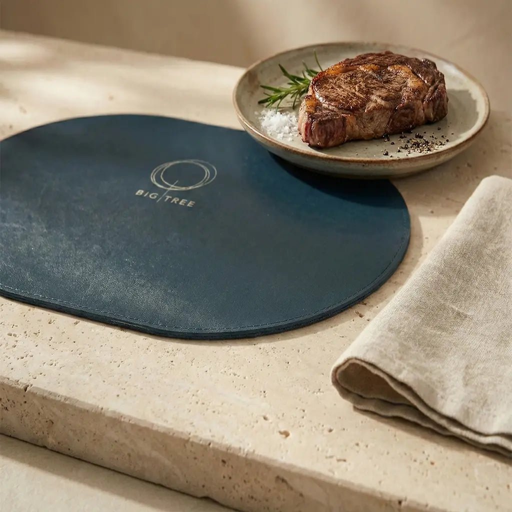 Blue placemat with a logo on a stone surface, next to a plate of steak.