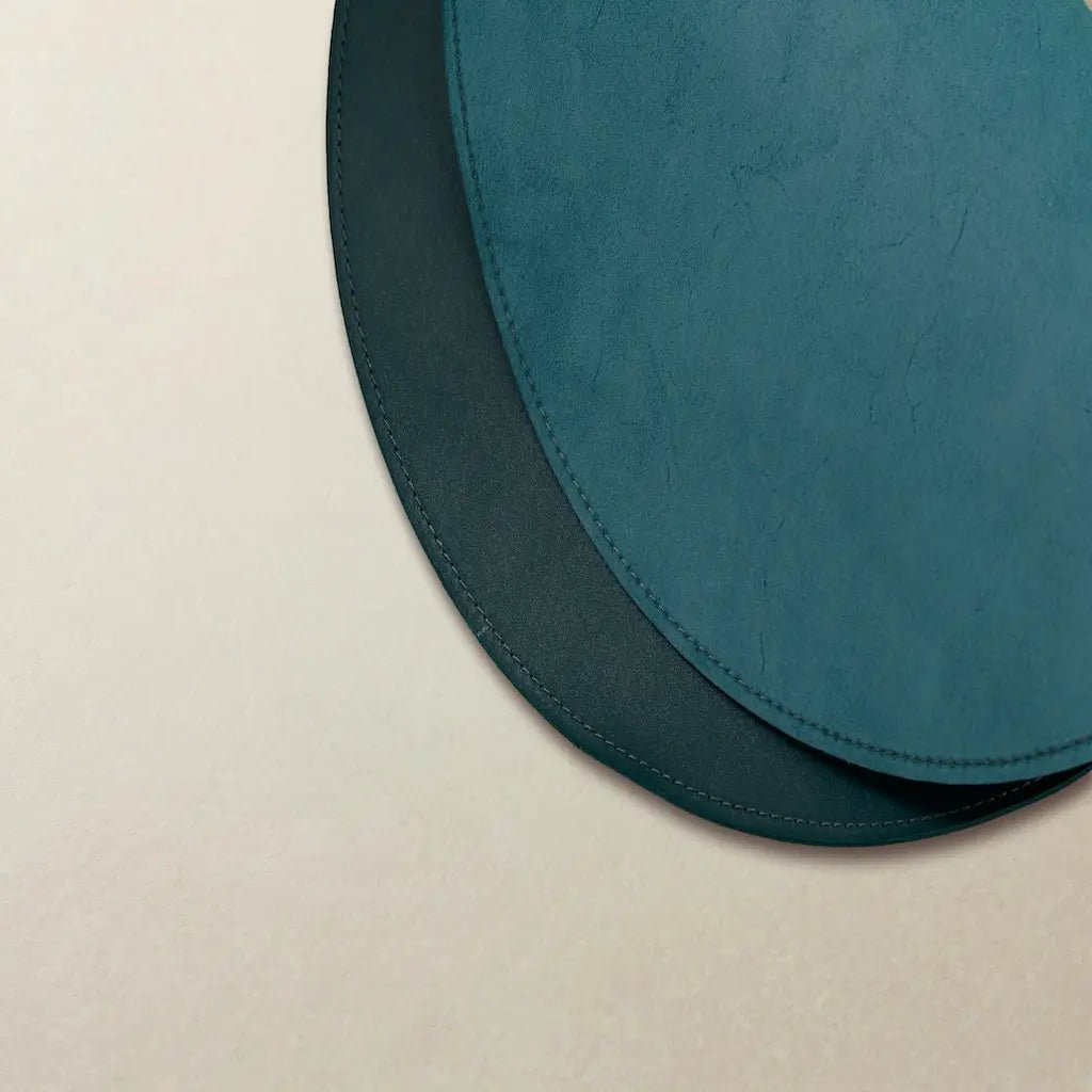 Two teal round placemats on a beige surface