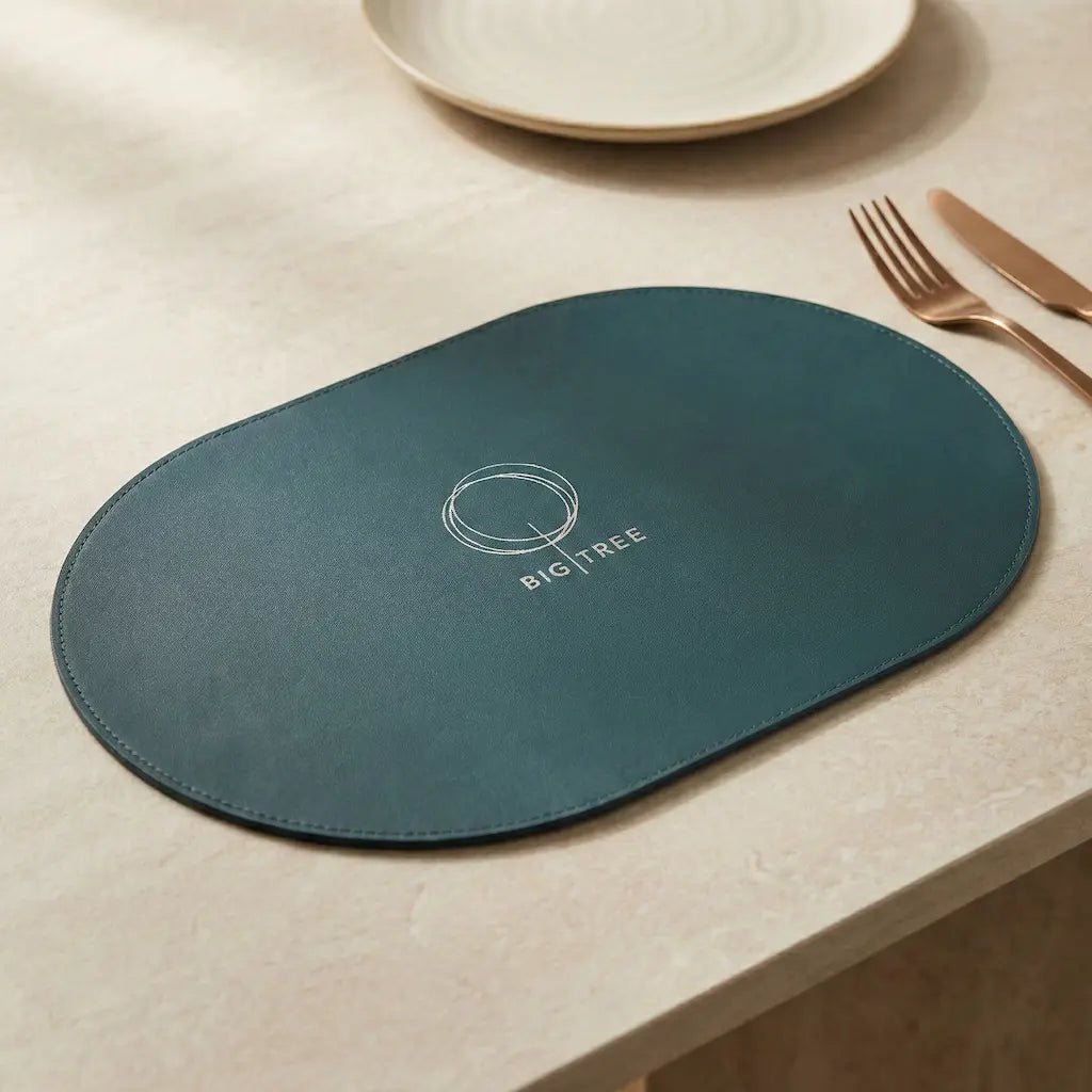 Teal placemat with 'BIG TREE' logo on a beige surface with cutlery.