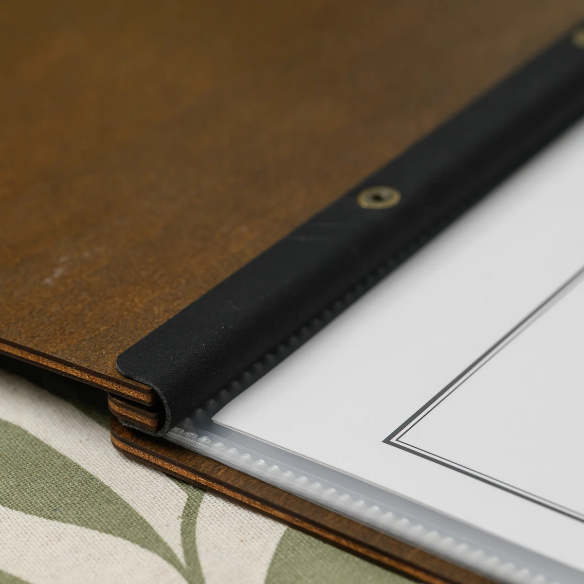 Close-up of brass screw heads on the wooden spine and black leather strap of a walnut plywood menu cover