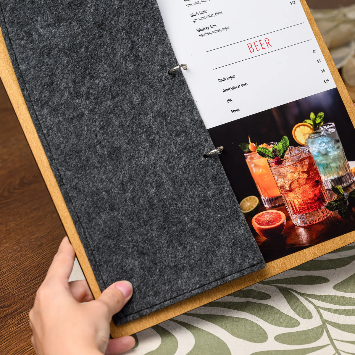 A hand holding open a ring-bound menu board, showing the felt cover folded back over a printed menu page 