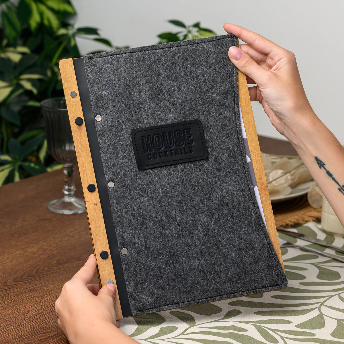 A hand holding a felt-covered menu folder to show the leather-bound wood spine up close, angled