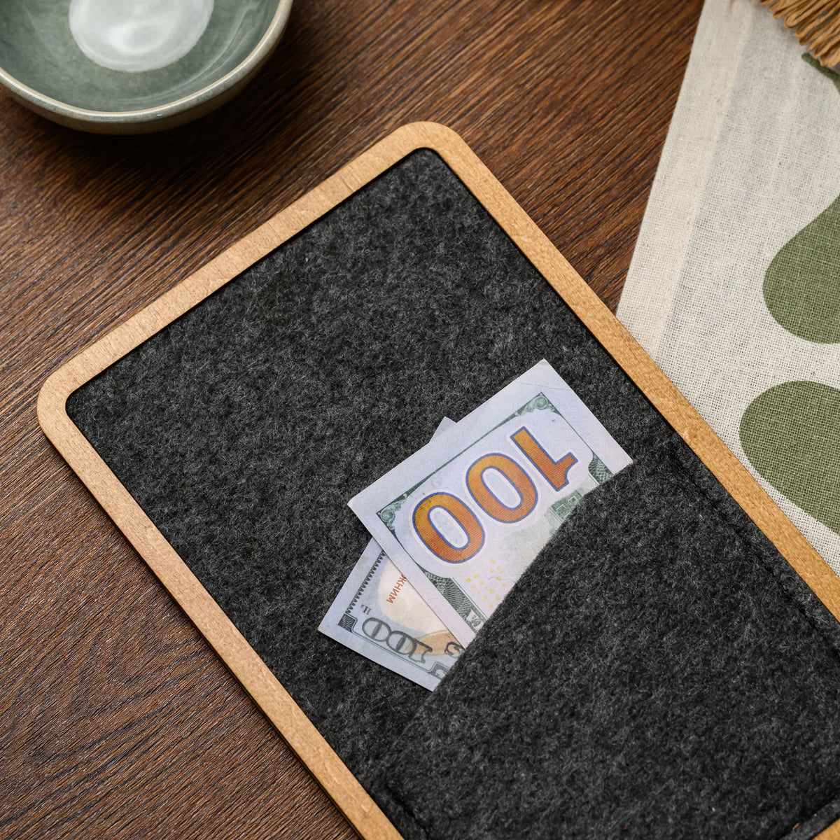 A close-up of a banknote tucked into the felt pocket of a wood-framed bill presenter, styled on a table 