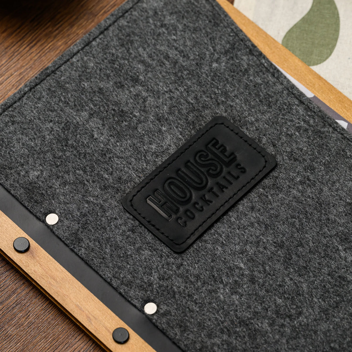 A close-up of a felt menu folder corner showing the leather patch and wood spine rivets in fine detail