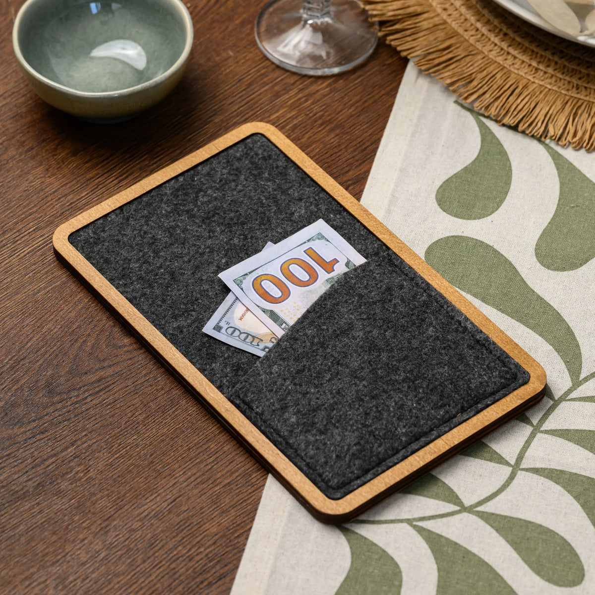 Wood-framed bill presenter with a banknote placed inside its felt pocket, seen closely 