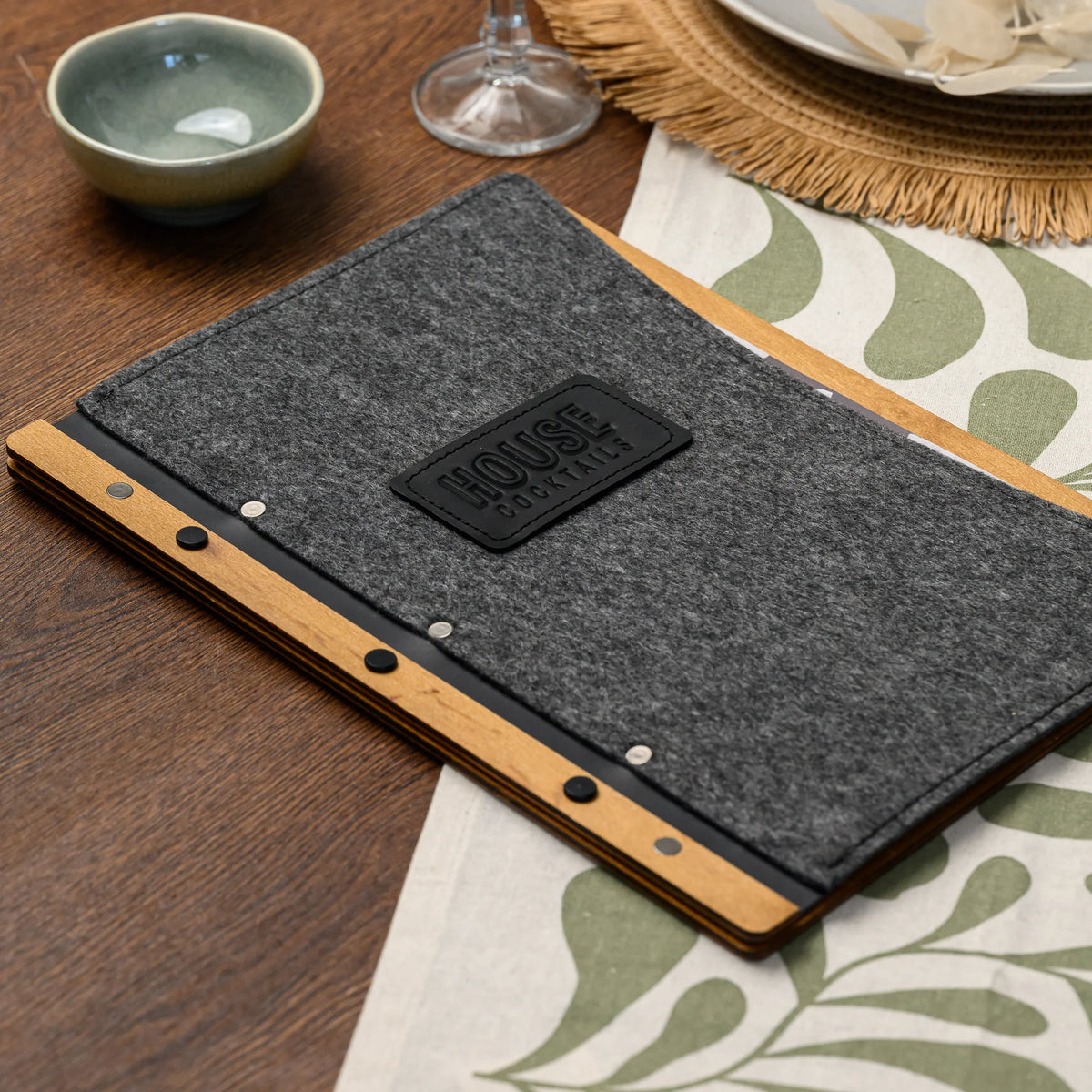 A closed felt-covered menu folder resting on a restaurant table near a ceramic bowl and place setting