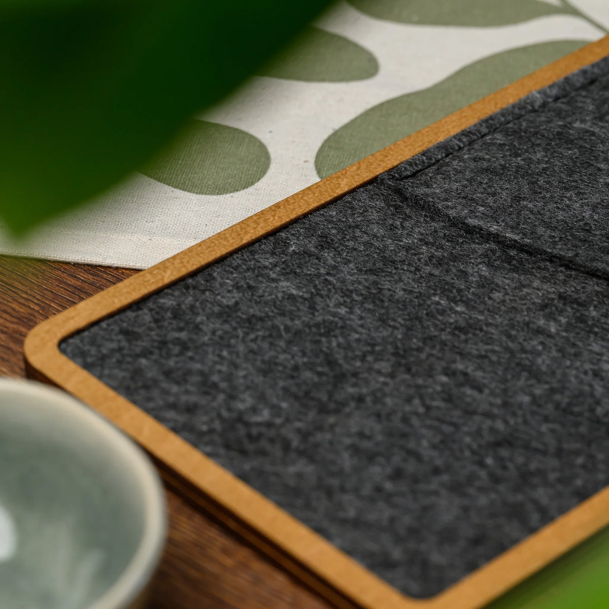 A macro view of the felt pocket and wood frame corner on a bill presenter, near a green leaf and cup 