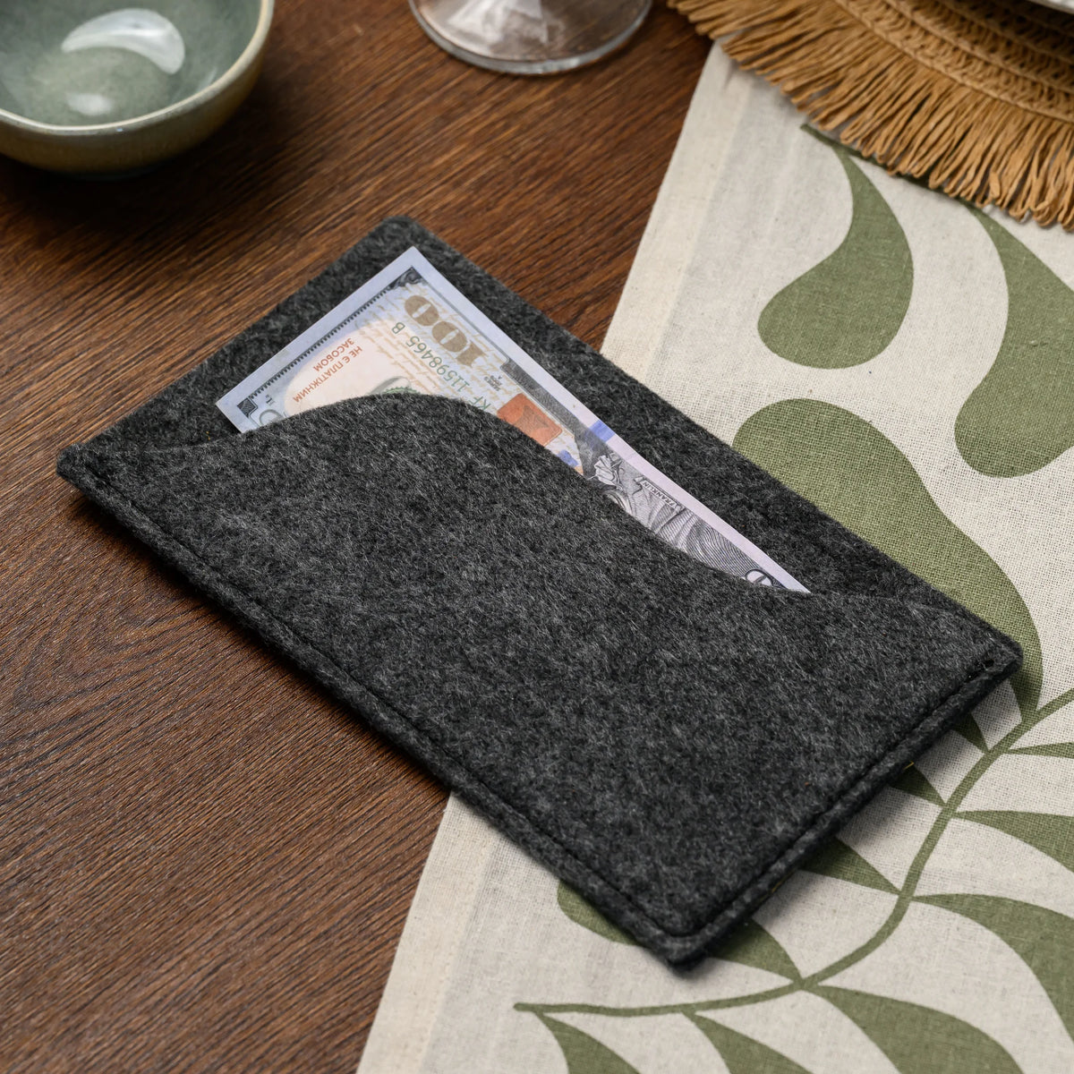 A close-up of a banknote tucked into the wavy-edged felt pocket of a bill presenter, on a wood table