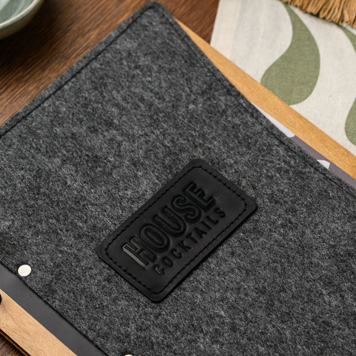 A close-up of an embossed leather patch centered on the felt cover, positioned next to a wood spine rivet