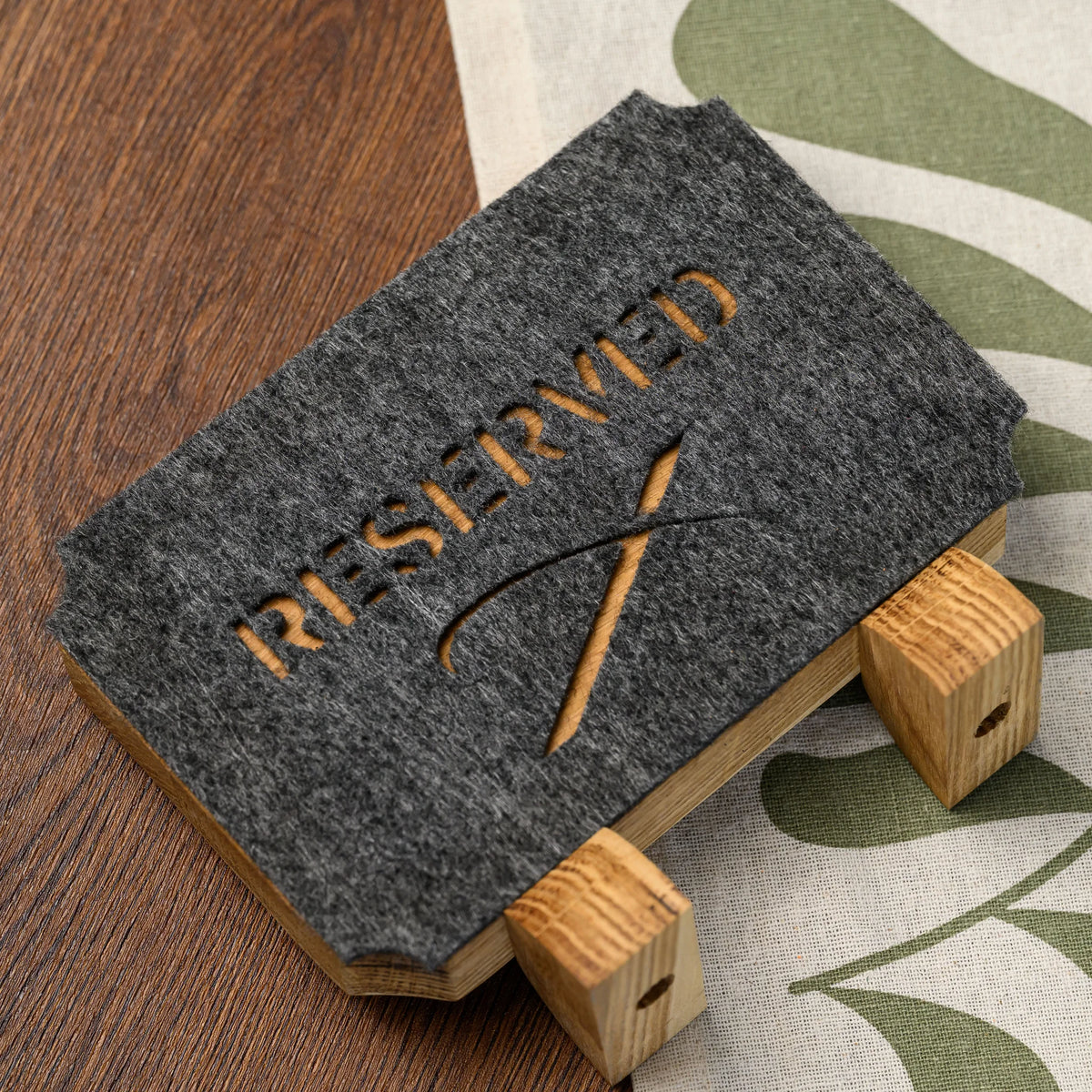 An overhead view of a Reserved table sign with felt cutout lettering resting on its two oak stand legs