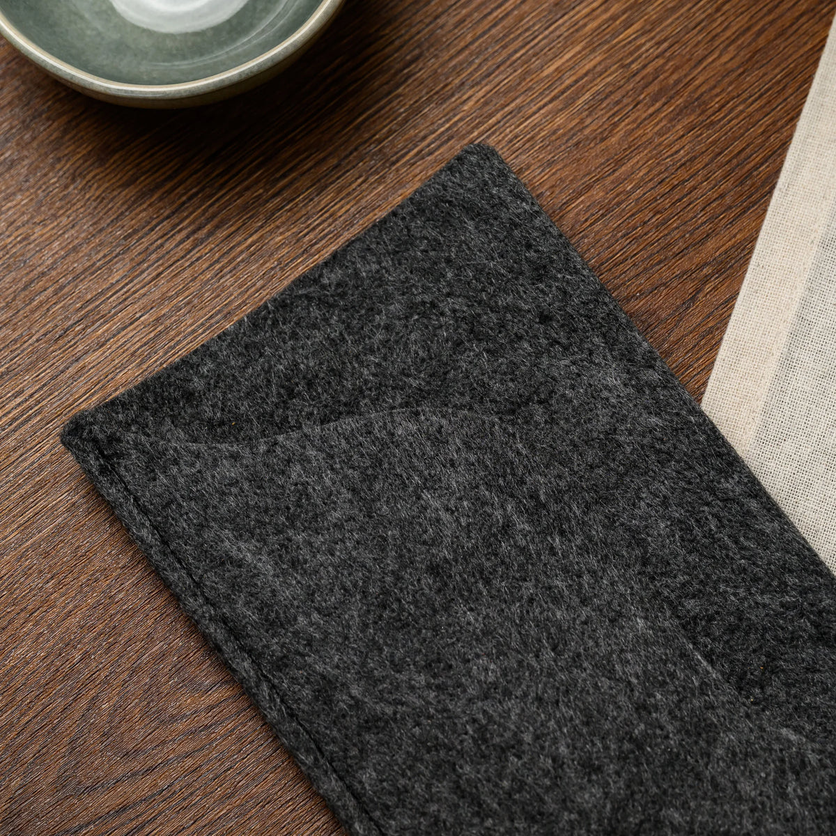 An overhead view of a folded felt bill presenter with its wavy pocket flap left open on the wood table 