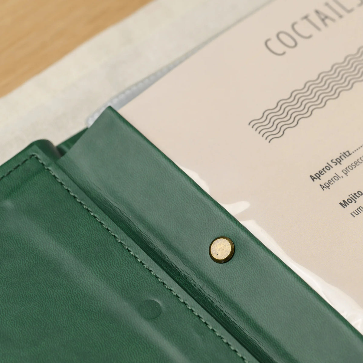 Close-up of an antique brass screw on the leather plank of a green menu cover next to a menu page in a clear sleeve