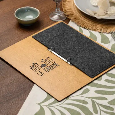 An engraved logo on the plywood front of a menu board, with the felt cover pocket resting close beside it 