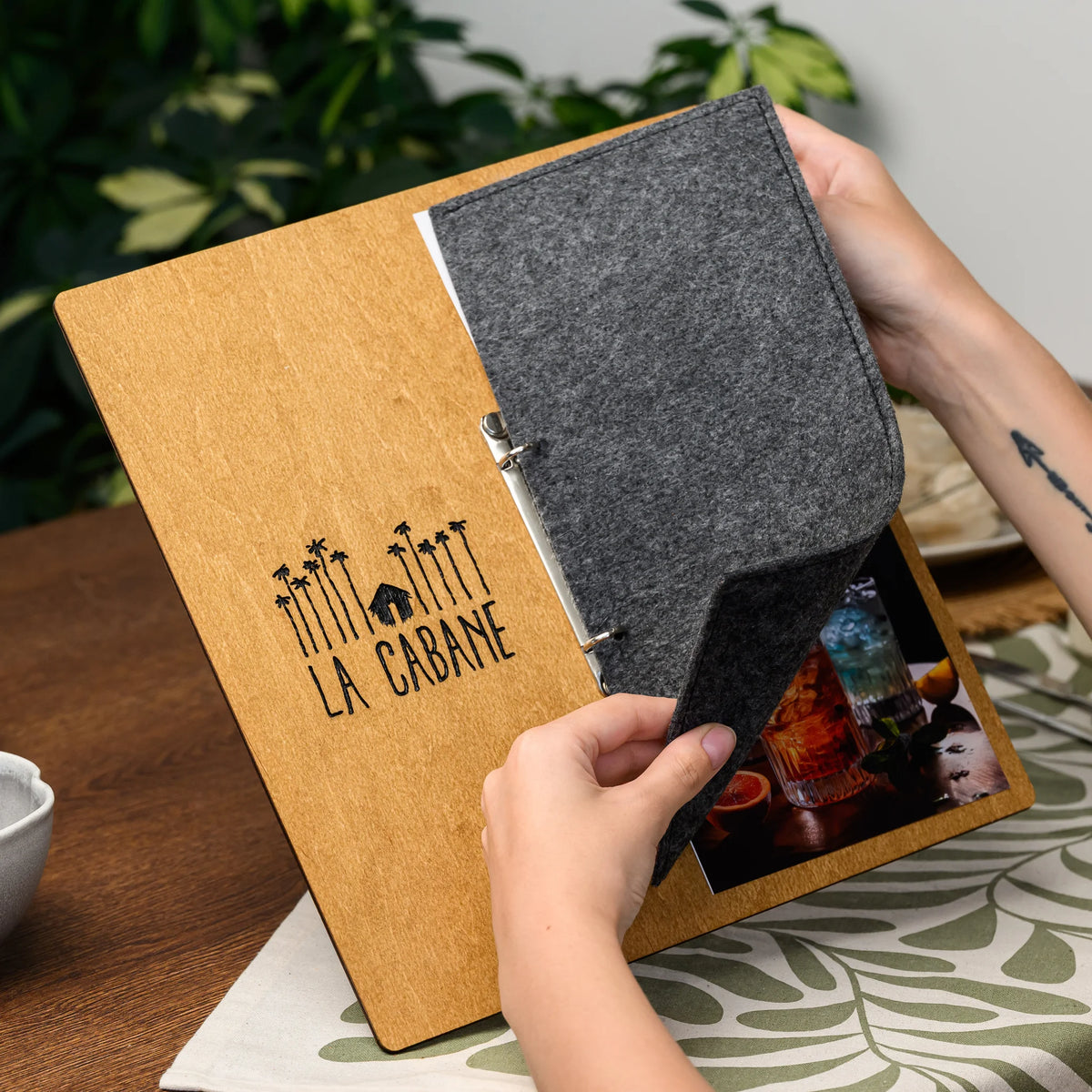 Hands holding open a menu board, showing the engraved plywood front and the felt cover folded fully back 