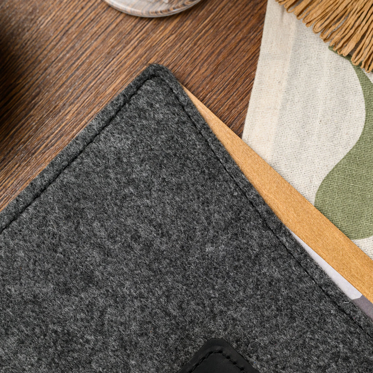 A macro view of a stitched felt cover corner and wood spine edge on the menu folder, near a linen napkin