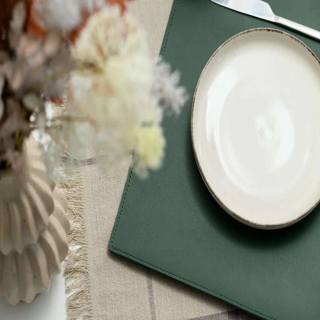 Table setting with a white plate on a green placemat, flowers, and a knife.