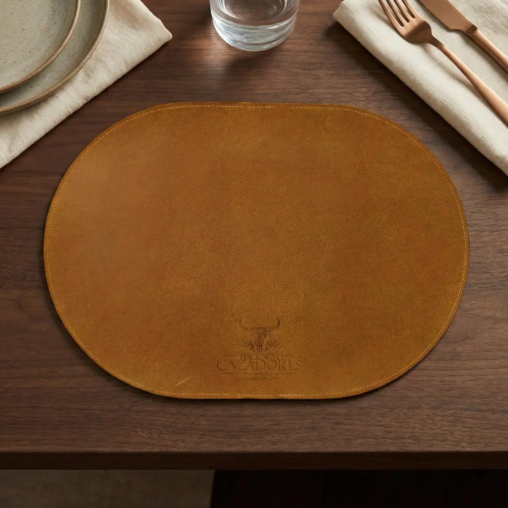 Brown leather placemat on a wooden table with cutlery and glassware.