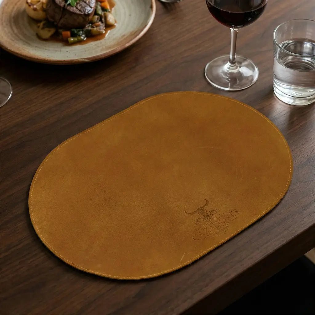 Brown leather placemat on a wooden table with a dish of food and glasses of wine and water.