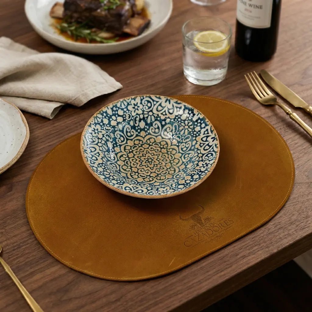 Decorative bowl on a brown placemat with a glass of water and lemon, wine bottle, and cutlery on a wooden table.