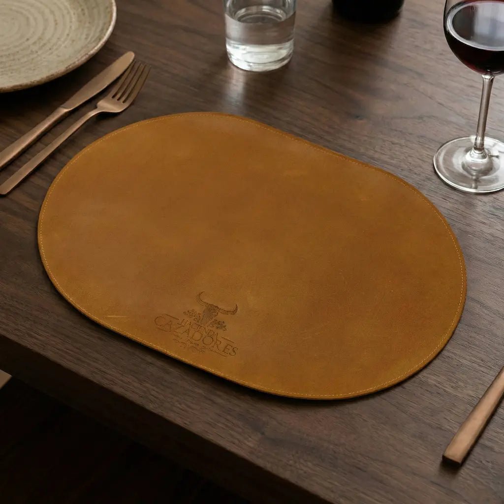 Brown leather placemat on a wooden table with cutlery and glasses.