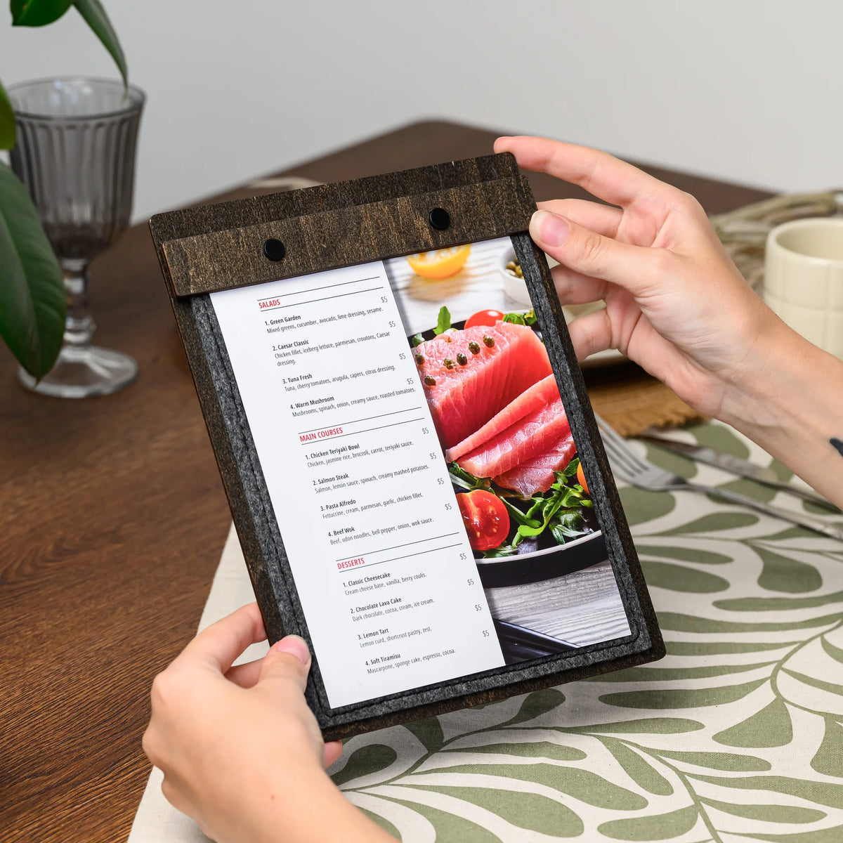 Hands holding a felt menu board that displays a printed menu page secured under its clamp bar closely 