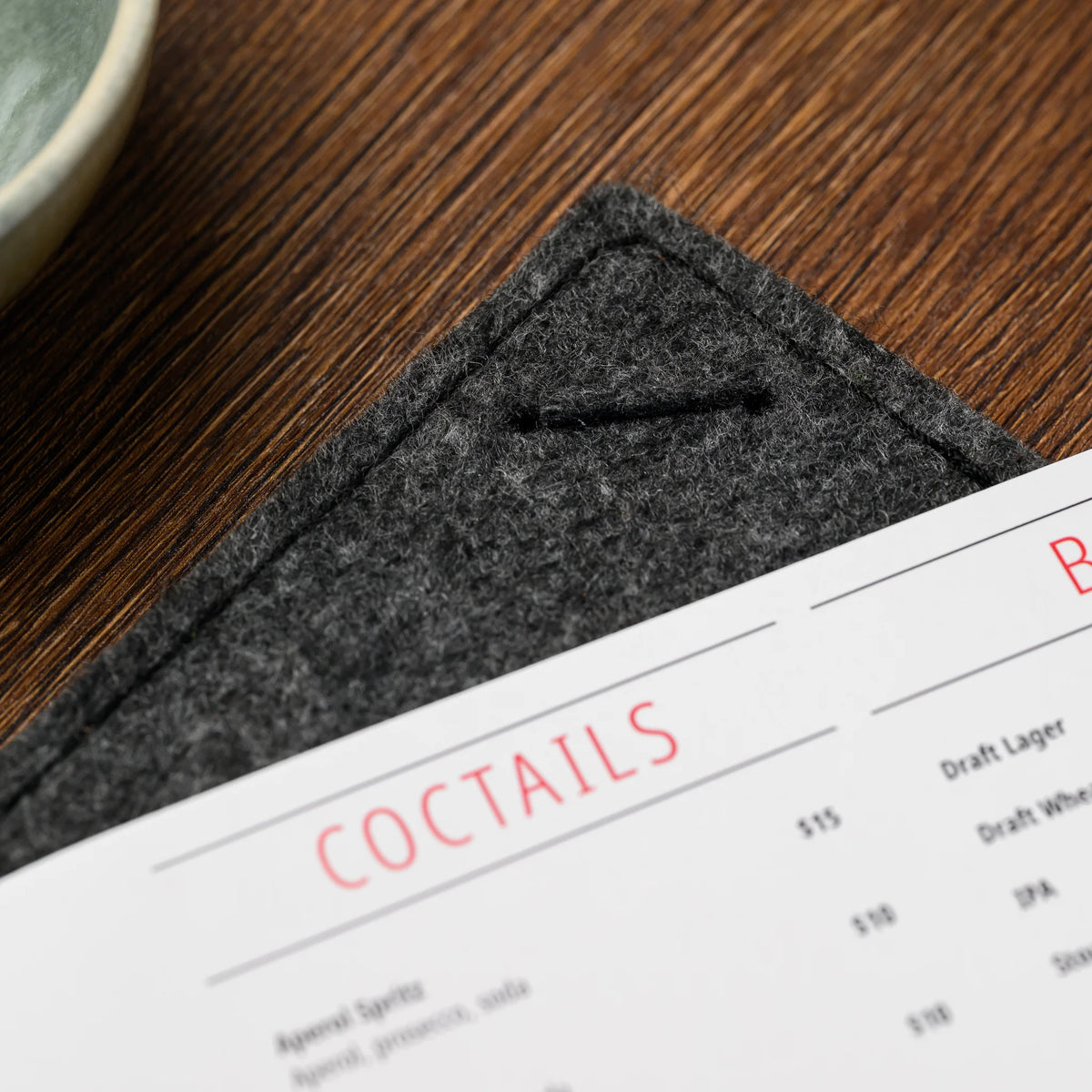A macro view of an empty corner slot on the felt menu clipboard, stitched into the fabric edge closely 