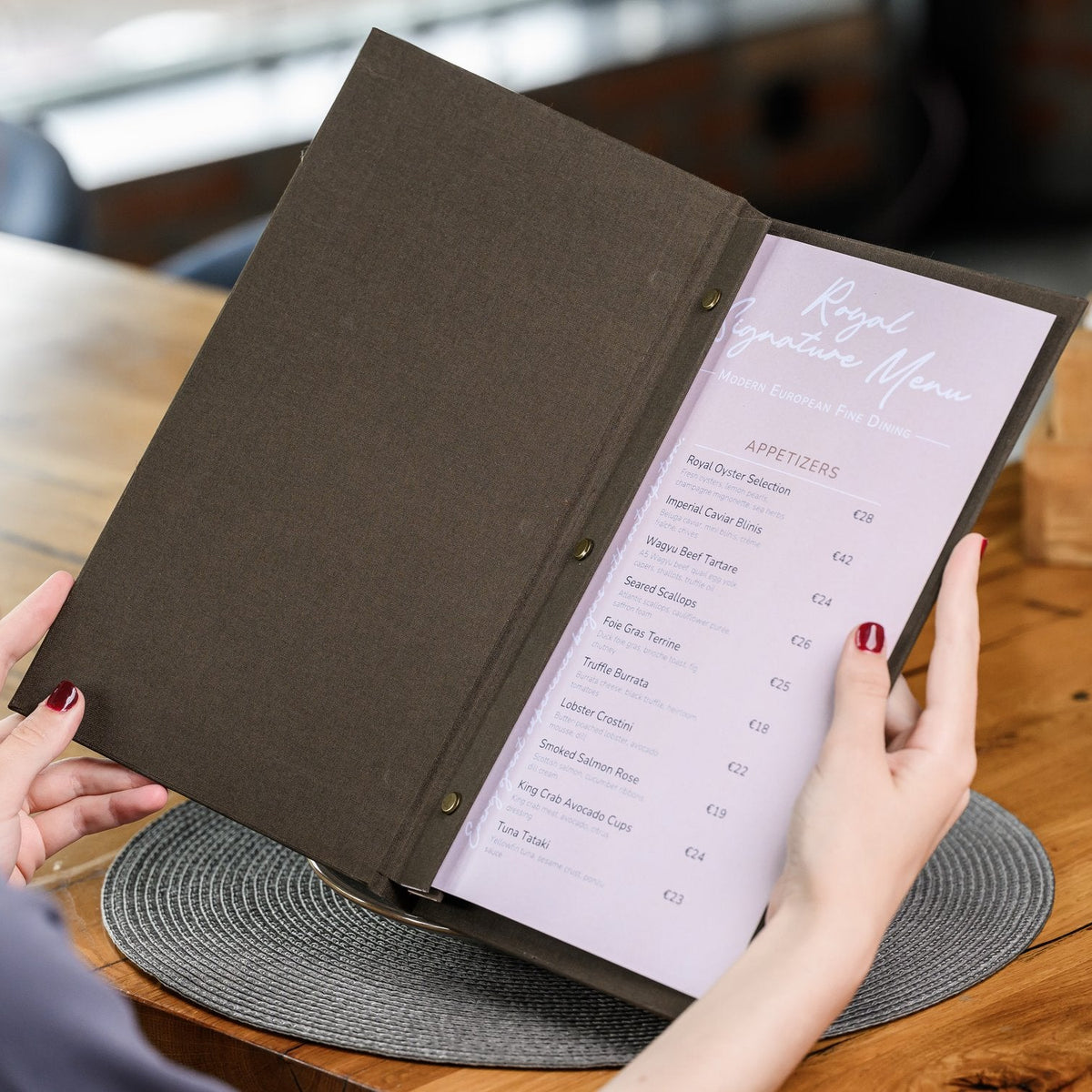 Hand holds a wide open espresso-brown textile menu folder with a lavender menu page on a wooden table
