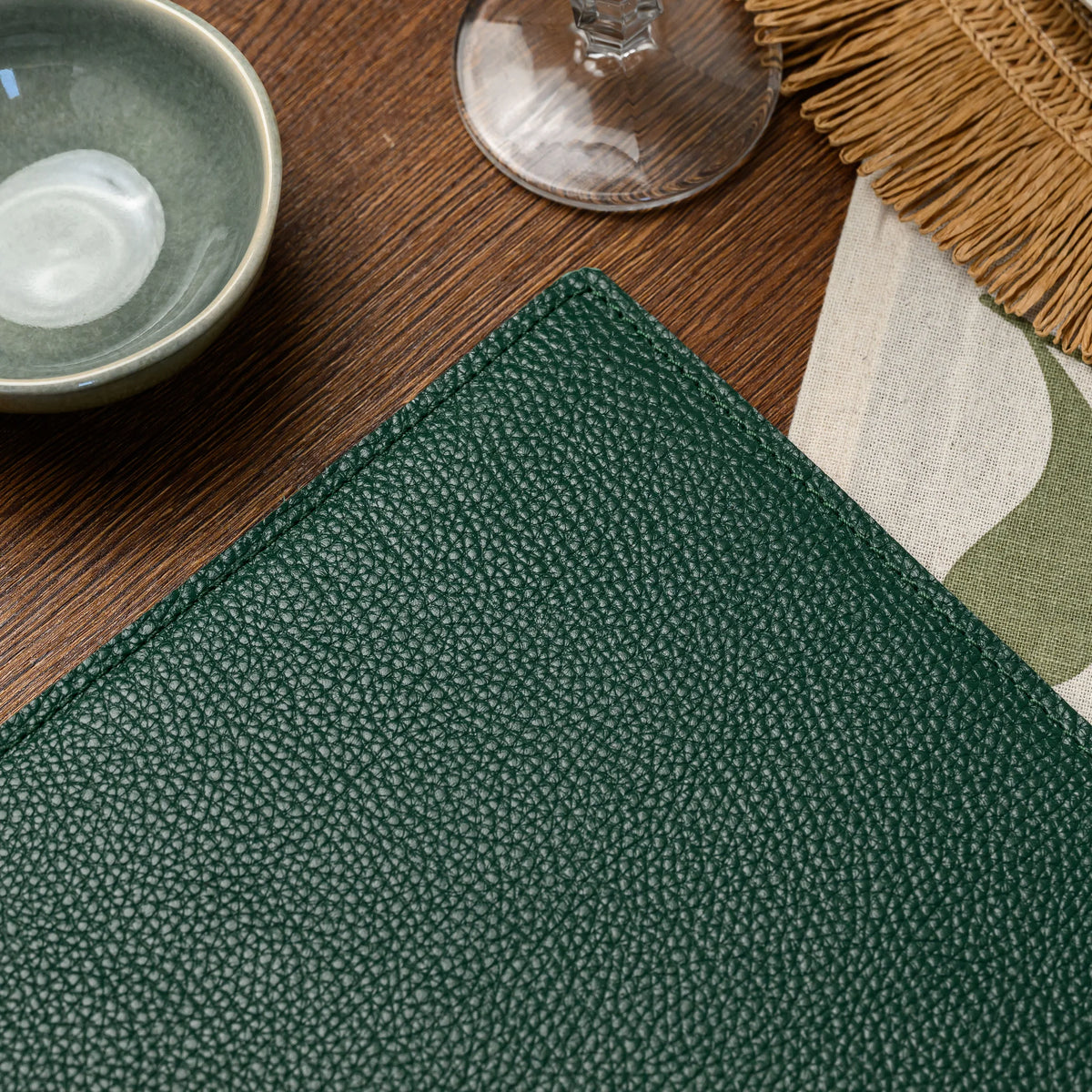 Close-up of green milled leather cover corner showing natural pebble grain and tonal stitching along the edge
