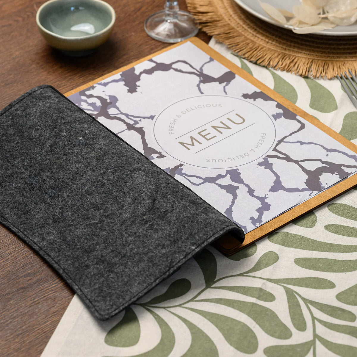 An open felt-covered menu folder displaying a printed menu insert on a fully set restaurant dining table