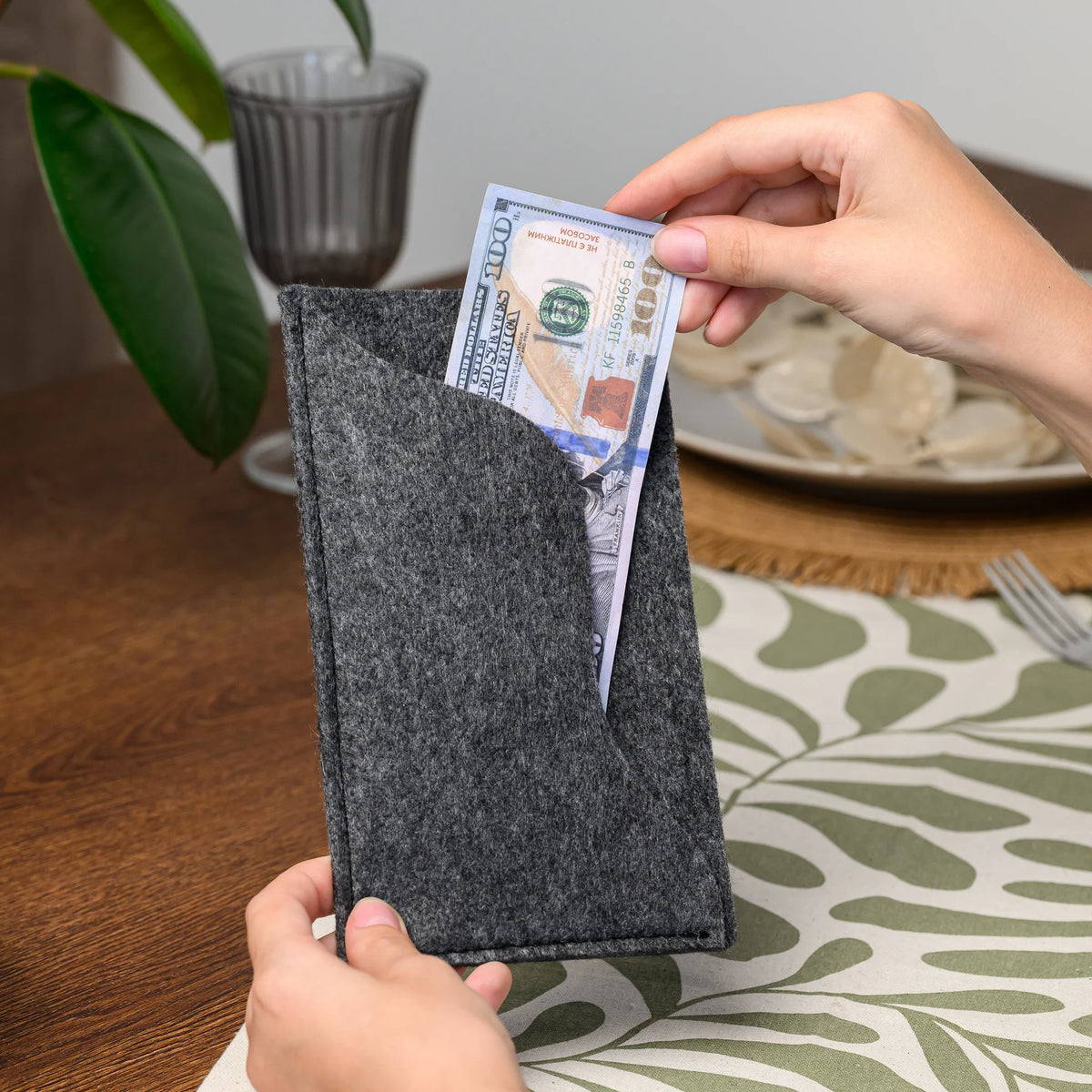 Hands pulling a banknote out of the wavy felt pocket of a bill presenter, held upright over the table