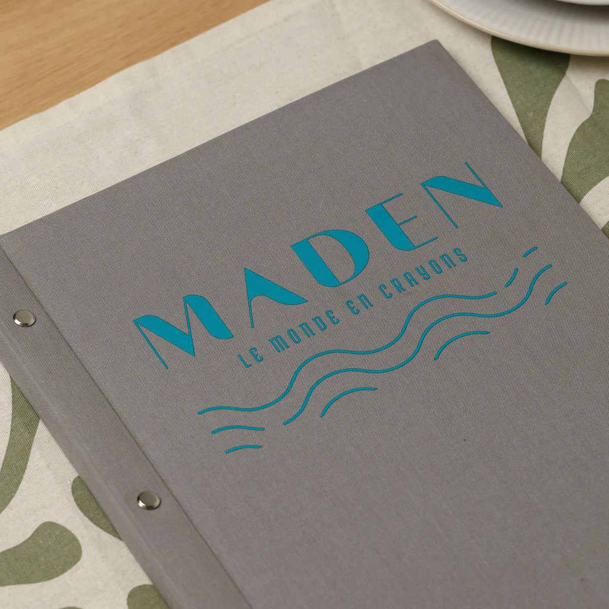 Close-up of a full-color DTF printed logo on the front of a gray fabric menu cover with chrome screw heads