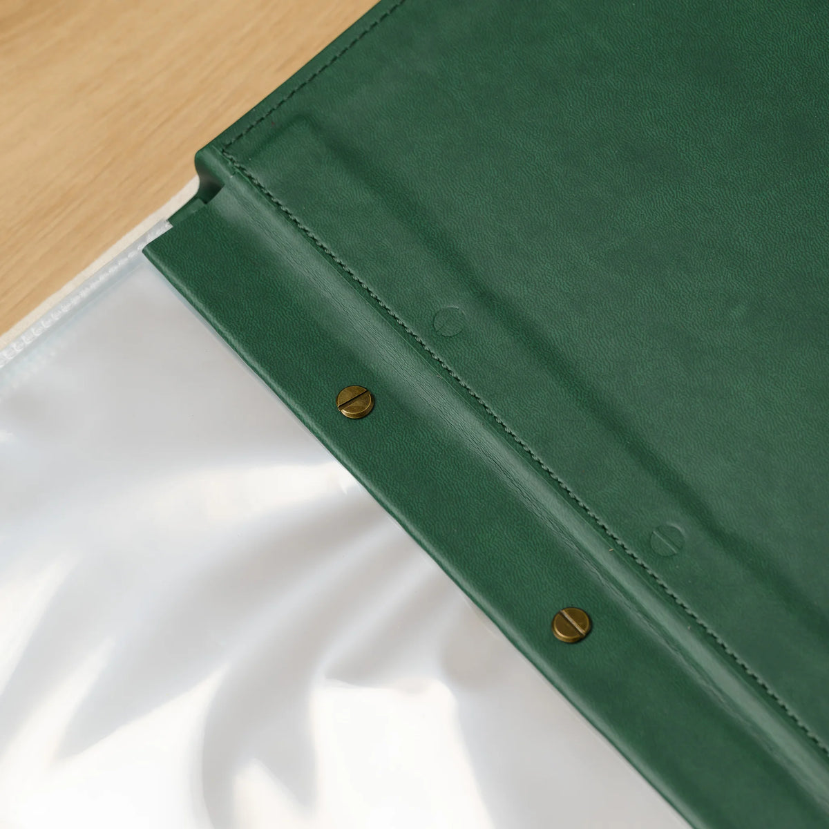 Outer spine of a green faux leather menu cover with two slotted brass screw heads above a stack of plastic sleeves
