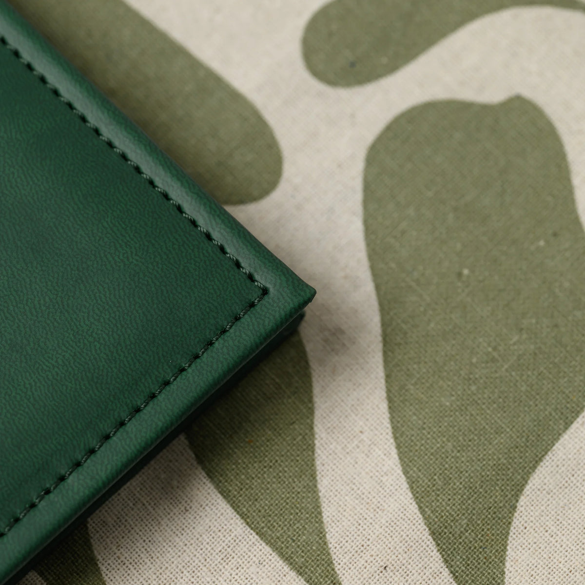Macro view of the stitched corner of a green faux leather menu cover showing the fine grain of the PU leather