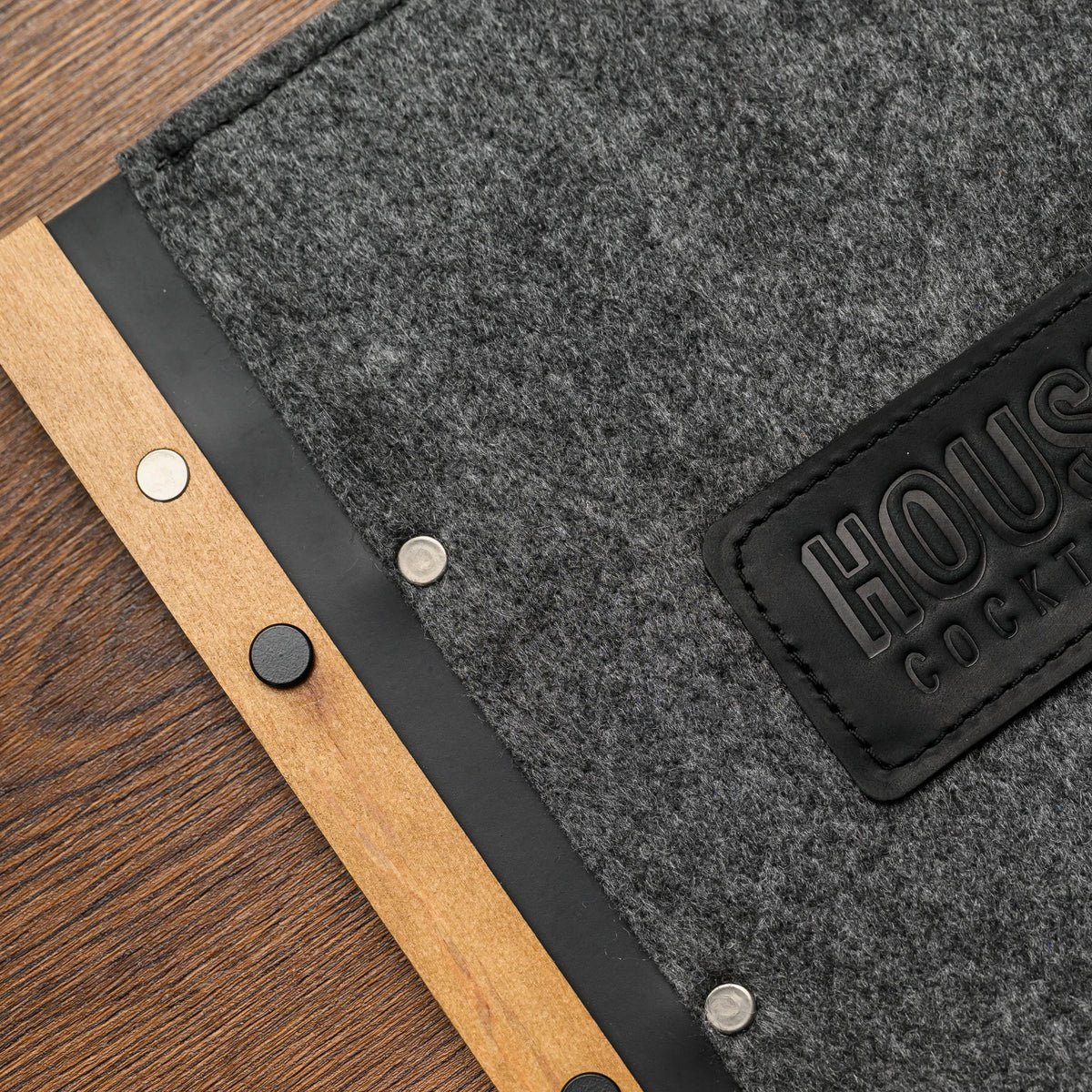 A flat lay close-up of the felt menu folder cover showing the embossed leather patch and wood spine edge